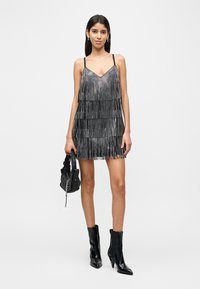 Μαύρο φόρεμα με φουντίτσες και λεπτές τιράντες, με στρωματοποιημένο σχέδιο και μεταλλικές λεπτομέρειες. Συνδυασμένο με μαύρες μπότες με ψηλό τακούνι και μικρή τσάντα.