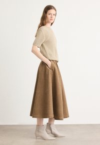 Beige kötött, rövid ujjú felső egy térdhosszúságú barna kordbársony szoknyával, oldalzsebekkel. Világos bézs magassarkú bokacsizma.