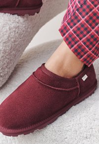 Scarpa slip-on color bordeaux in morbido suede con superficie testurizzata e suola in gomma, caratterizzata da un bordo cucito e una piccola etichetta del marchio.
