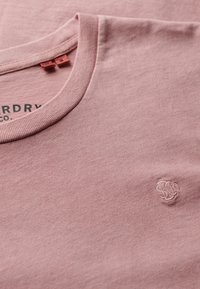 Roze katoenen T-shirt met ronde hals, voorzien van een gestructureerde afwerking en een subtiel geborduurd logo op de borst. Soepele stof.