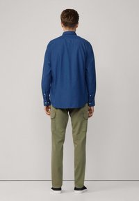 Camisa de botones de manga larga azul con cuello, combinada con pantalones cargo color oliva que cuentan con bolsillos laterales y un ajuste slim.