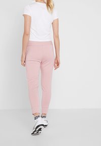 Ljusrosa joggers med avsmalnande ben och elastisk midja, kombinerat med en enkel vit T-shirt, visad från baksidan.