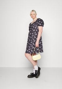 Vestido preto com estampado de borboletas brancas, mangas curtas bufantes e saia rodada. Acompanhado de uma pequena mala amarela e sapatos pretos.