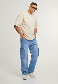 Beige oversized t-shirt with short sleeves, paired with light blue cargo pants featuring side pockets and white sneakers.