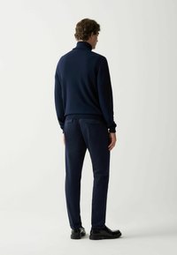 Jūras spēku zilo džemperi ar augstu apkakli, strukturētu audumu, saskaņots ar taisnas griezuma ziliem biksēm un spīdīgām melnām kurpēm. Vienkāršs, moderno dizains.