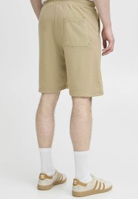 Shorts en kaki avec une taille élastique, une poche arrière et une texture lisse, accompagnés de baskets beiges et de chaussettes blanches.