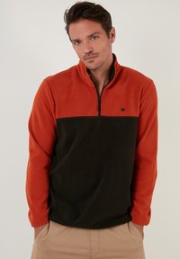 Fleece pullover with a quarter zip; orange top half and black bottom half; features a small logo on the chest; soft material.