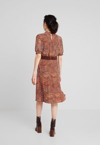 Bruine en oranje gestreepte jurk met puffmouwen, een cinched taille en een vloeiende rok. Gecombineerd met bruine enkellaarzen. Achteraanzicht.