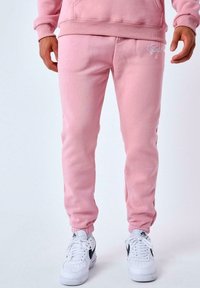 Pantalones de chándal de algodón rosa con un corte ajustado, puños de canalé y un acento de logo en el muslo, combinados con zapatillas blancas.