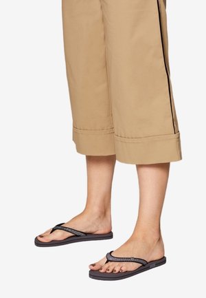 Chanclas negras con una tira texturizada, que presentan una suela plana y un diseño minimalista. Combinadas con pantalones cortos caqui.