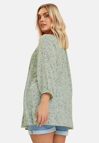 Ljusgrön blus med blommönster, trekvartsärmar och lös passform, ihop med rullade denimshorts. Mjuk, texturerad tyg.