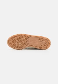 Shoe outsole with a textured, rubber material in light brown. Features circular patterns and branding "adidas" in clear letters.