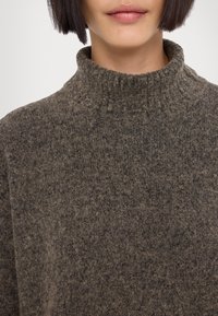 Pull marron à col montant en tissu tricoté texturé. Caractérisé par un col côtelé et une apparence douce et duveteuse, avec une coupe ample.