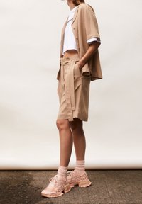 Beige button-up shirt and tailored shorts, featuring a belted waist. White crop top underneath. Light pink sneakers with textured accents.