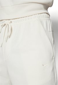 Baltos sportinės kelnės, pagamintos iš minkštos, tekstūrinės medžiagos. Turi elastinį juosmenį su raišteliu ir mažą sidabrinę Nike logotipą šone.