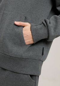 Szara bluza z kapturem wykonana z miękkiego materiału, z kieszenią kangurką i ściągaczami na rękawach. Ma małą metkę z logo na bocznym szwie.