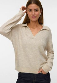 Beżowy sweter dzianinowy z dekoltem w serek i kołnierzykiem, z długimi rękawami i prążkowanymi mankietami. Tekstura wydaje się miękka i lekko melanżowa.