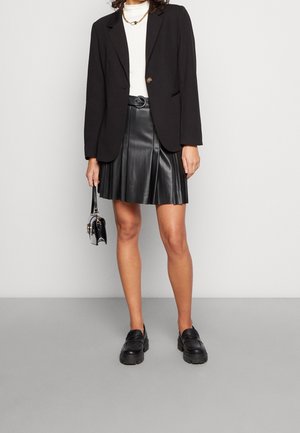 Svart blazer med en knapp, kombinerad med en plisserad svart skinnkjol. Svarta kraftiga loafers och en liten svart handväska fulländar looken.