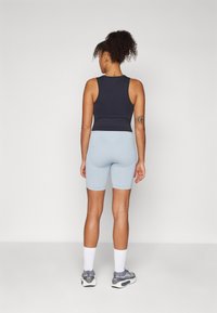 Svart ermeløs topp, lyseblå sykkelshorts, ankellange hvite sokker og grå sportssko, sett fra baksiden. Glatte stoffer.