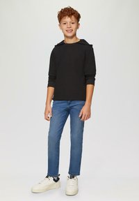 Czarny sweatshirt z kapturem i długimi rękawami, zestawiony z niebieskimi dżinsami i białymi trampkami. Materiał wydaje się miękki i ma luźny krój.