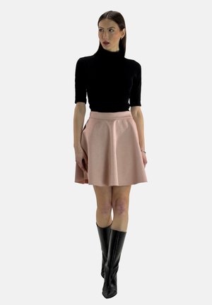 Schwarzes, enges Rollkragenoberteil, kombiniert mit einem hellrosa ausgestellten Rock. Das Outfit wird durch knielange schwarze Stiefel ergänzt.