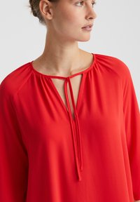 Rote, leichte Bluse mit einem runden Ausschnitt und Bindeband, die an den Schultern geraffte Details und lange Ärmel aufweist.
