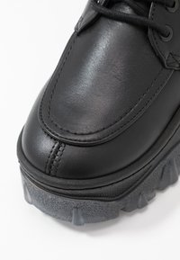 Czarne skórzane buty o gładkim wykończeniu, z grubą, teksturowaną szaro-skalą i widocznymi szwami wzdłuż palców. Sznurowadła są czarne.