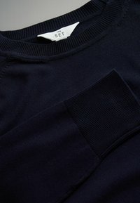 Námornícký svetr s dlouhým rukávem a kruhovým výstřihem, s žebrovaným límcem a texturovanou kapsou na přední straně. Vyrobeno z jemné, lehké látky.