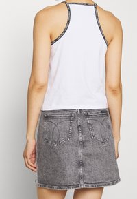 Top cropped bianco con bordi neri che presenta un logo, abbinato a una mini gonna in denim grigia con tasche posteriori e un orlo leggermente sfilacciato.