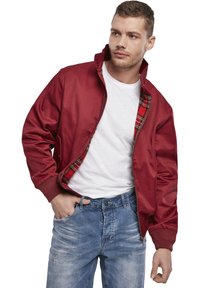 Veste bombardier rouge avec doublure à carreaux, poignets et col côtelés. Portée sur un t-shirt blanc et associée à un jean bleu. Coupe décontractée.