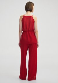 Conjunto ligero y holgado en rojo, que incluye una blusa de malla y pantalones de pierna ancha, ambos con un acabado texturizado y cinturilla ajustable.