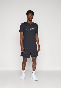 Svart Nike t-skjorte med hvitt logo, kombinert med svarte shorts. Båret med hvite joggesko og ankelsokker, som viser et avslappet atletisk utseende.