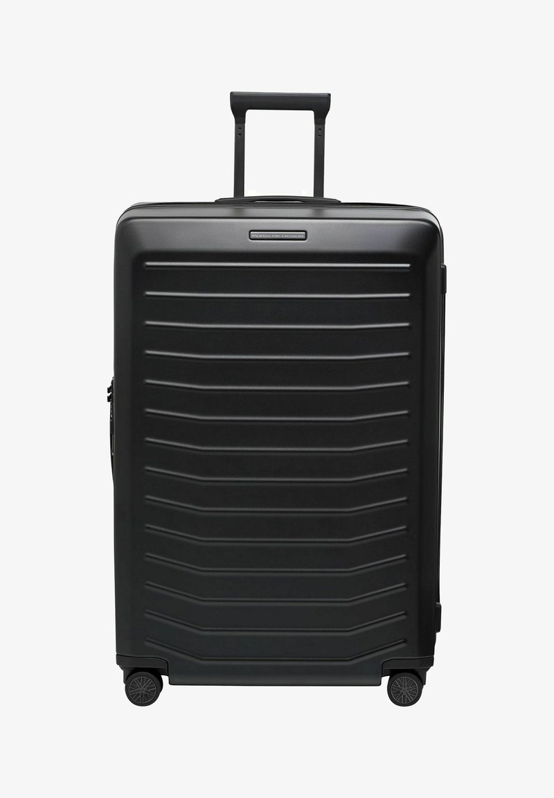 Valigia rigida nera con superficie textured e scanalature orizzontali, manico retrattile e quattro ruote per la mobilità.