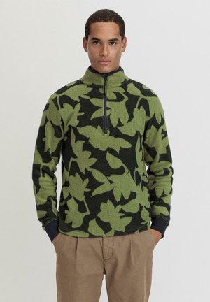 Fleece-Pullover in grünem und schwarzem Blumenmuster, mit hohem Kragen, halben Reißverschluss und gerippten Bündchen. Weiche Textur.