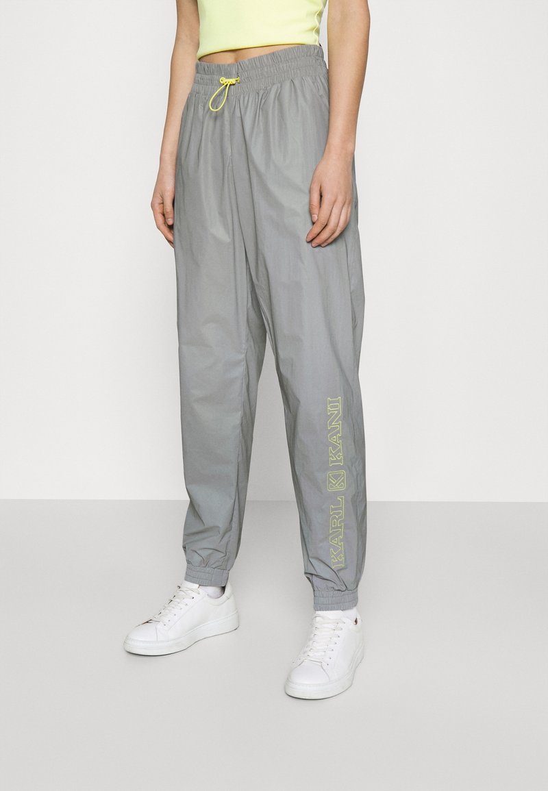 Graue, leichte Jogginghosen mit elastischem Bund und verstellbarem gelben Kordelzug. Mit seitlichem Logo in hellgrün. Bündchen an den Knöcheln.