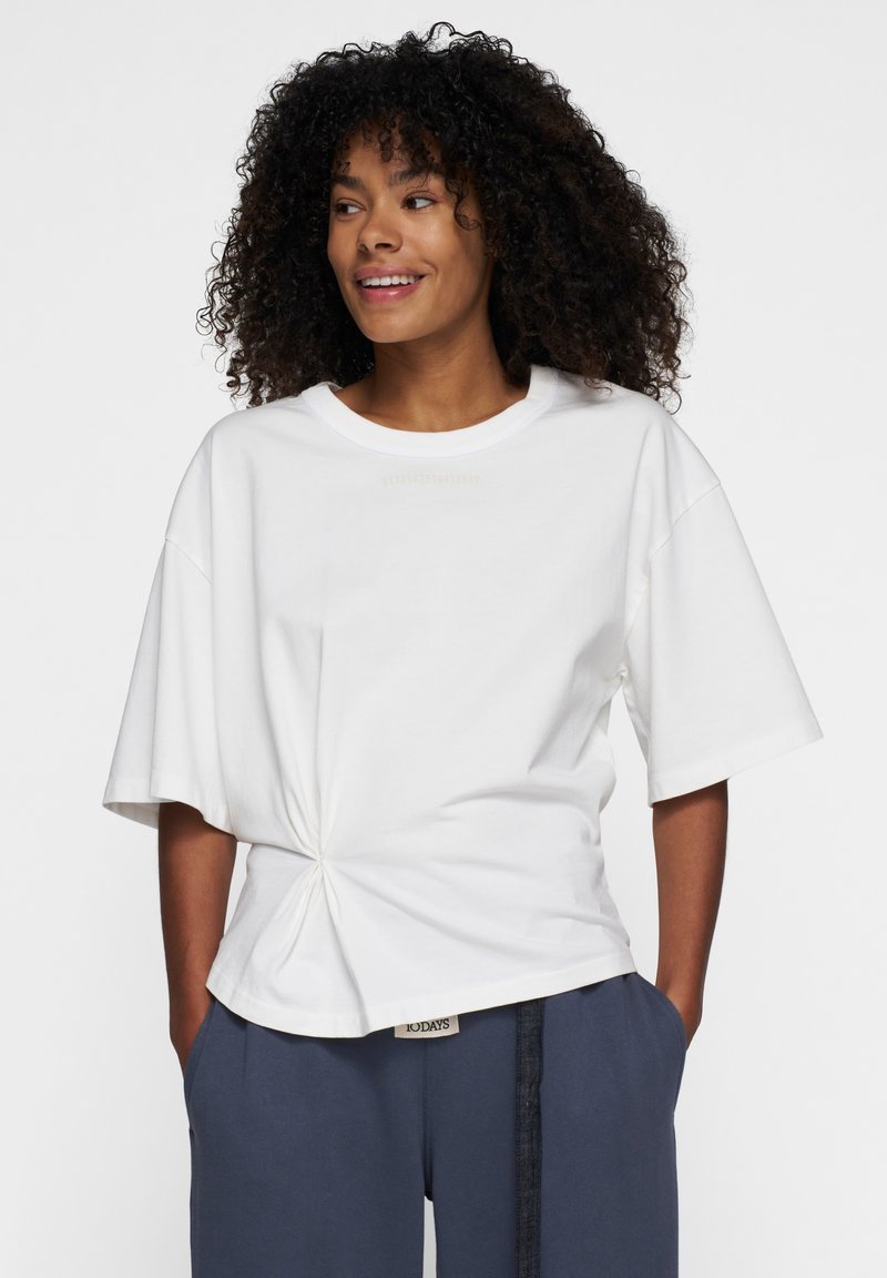Witte katoenen t-shirt met ronde hals, korte mouwen en gedraaide details aan de zoom. Eenvoudig ontwerp, label aan de onderkant.