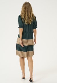 Kladna obleka z nabranimi kratkimi puff rokavi, temno zelenim zgornjim delom in bež črtastim krilom. Tkanina ima gladko teksturo in oblikovan pas.