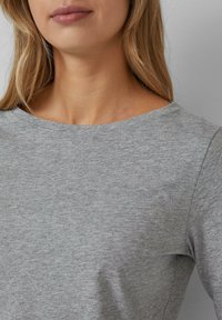 Haut gris à col ras du cou en tissu lisse et légèrement texturé. Présente des lignes épurées et un design simple, sans décorations, adapté à une tenue décontractée.