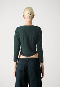 Tumedat rohelised, kehafiguuriga pikkade varrukatega särk ümarate kaelustega, koos kõrge vöökohaga mustade cargo-pükstega, millel on tagakotid.