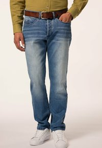 Vaqueros de denim azul claro con un lavado desgastado, corte slim, cinco bolsillos y cinturón de cuero marrón, combinados con zapatillas blancas.