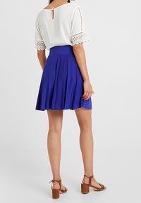 Blue pleated skirt with a high waistband, paired with a white blouse featuring lace accents and a keyhole back detail.