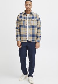 Geruite flanellen overhemden in beige, blauw en grijs met twee borstzakken, gecombineerd met marineblauwe broeken en witte sneakers. Rechte pasvorm en knoopsluiting.