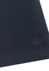 Tissu bleu foncé avec une texture côtelée fine montrant un ourlet cousu et un logo 4F embossé subtil près du bord inférieur.