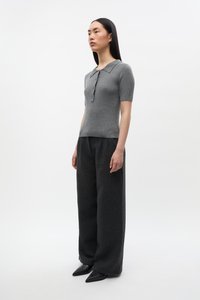 Sivý pletený polokošeľa s krátkymi rukávmi, v kombinácii s voľnými tmavosivými nohavicami a špicatými čiernymi topánkami. Minimalistický dizajn, textúrovaná látka.