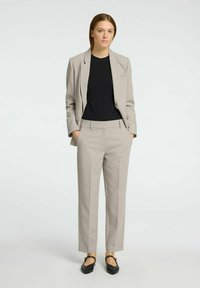 Grå skræddersyet blazer over en sort top, parret med matchende grå bukser og sorte flade sko. Glat stof med en struktureret pasform.