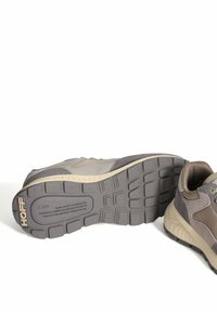 Une paire de baskets décontractées grises et beiges, l'une posée sur le côté montrant la semelle à motifs avec la marque "HOFF".