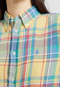 Camicia a quadri multicolore in giallo, verde, blu e rosso. Presenta un colletto button-down e un logo ricamato sul petto. Materiale in misto cotone.