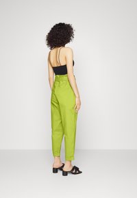 Groene, hooggeplaatste broeken met een losse pasvorm, voorzien van zijzakken en opgerolde boorden, gecombineerd met zwarte sandalen met blokhak en bandjes.