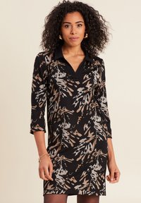 Langärmliges Kleid aus schwarzem Stoff mit einem Leopardenmuster in Beige, Grau und Braun. Es hat einen kragenförmigen Ausschnitt und eine Länge bis zur Mitte des Oberschenkels.