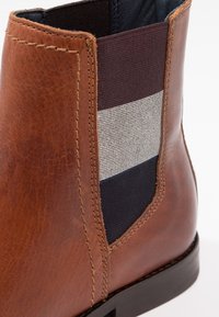 Bottine en cuir marron avec panneau latéral élastique présentant des rayures horizontales noires, grises et bleu marine, ainsi que des coutures apparentes.